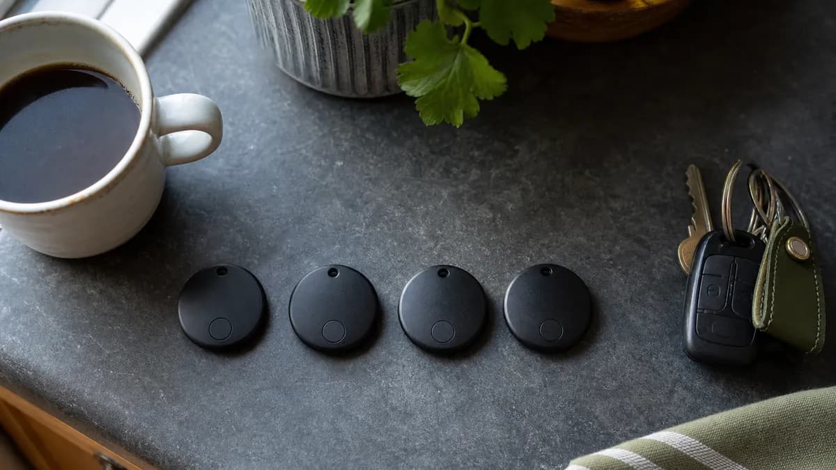 Several black tracking tags laid out in a row on a grey slate worktop beside a coffee cup and car keys