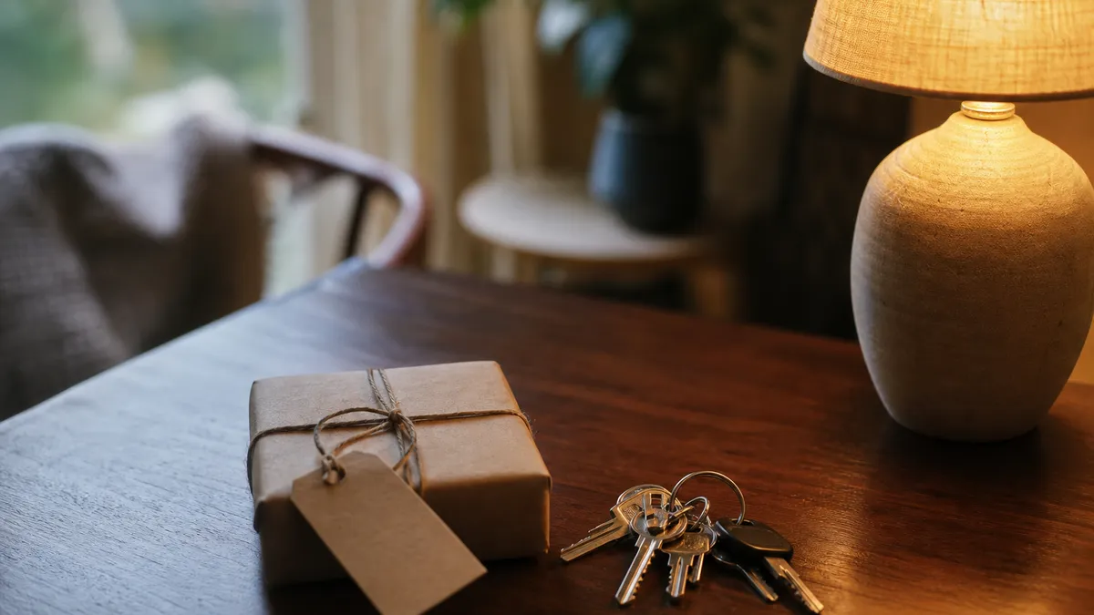 A small wrapped present with a plain paper tag resting beside a bunch of keys on a dark tabletop